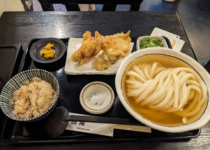 An udon set meal at Sanukiudon Byakuan, featuring udon noodles in a broth, rice, tempura, and toppings.